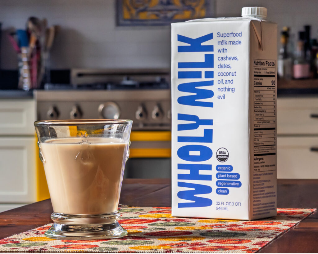 Wholy M!lk organic plant-based milk carton with a glass of milk on a kitchen table.