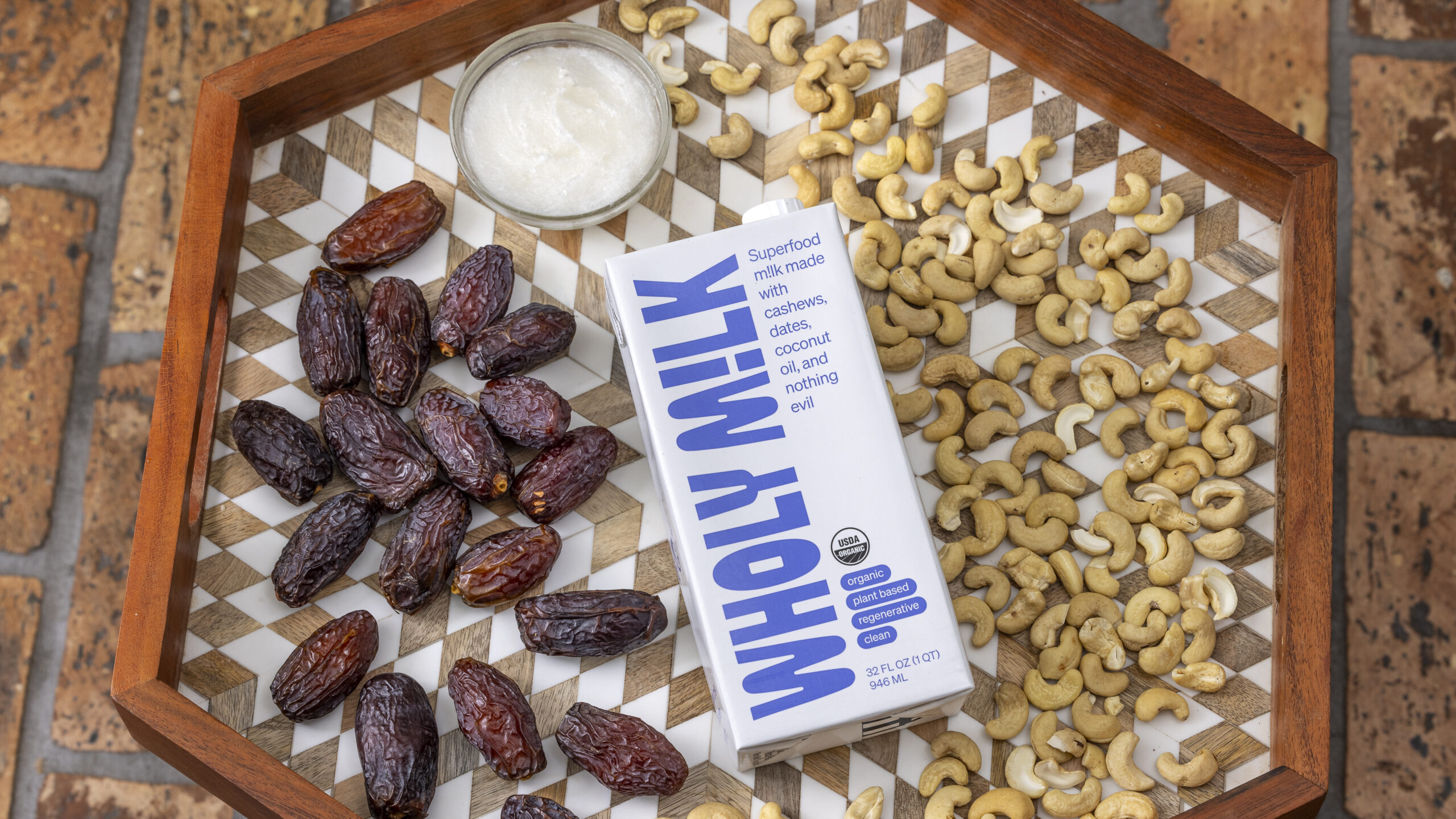 A carton of Wholy M!lk surrounded by organic dates, cashews, and coconut oil, highlighting its clean-label nutrition.