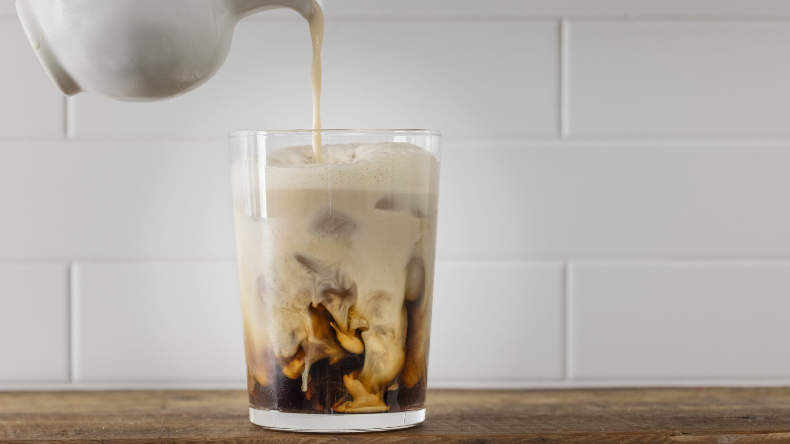 Wholy M!lk being poured into an iced coffee, showing its creamy texture and premium flavor.